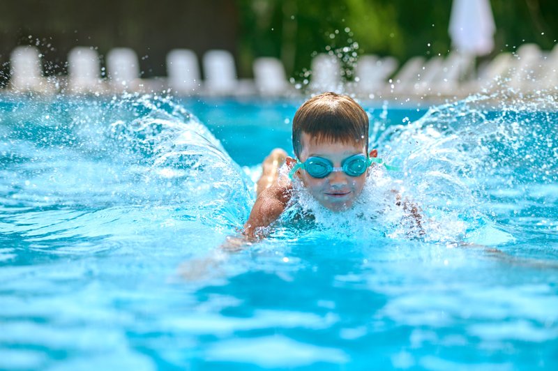 Garçon avec lunettes de natation pratiquant la brasse dans une piscine en Suisse