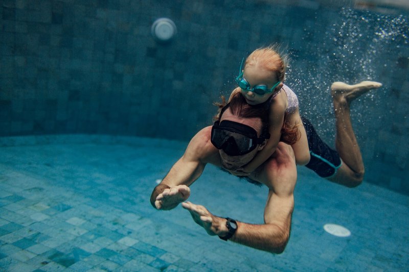 Un père apprend à nager à sa fille sous l’eau dans une piscine en Suisse